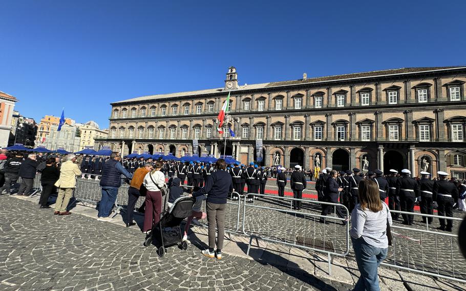 The crowd looks on as military service members in uniform gaze up at the Italian flag